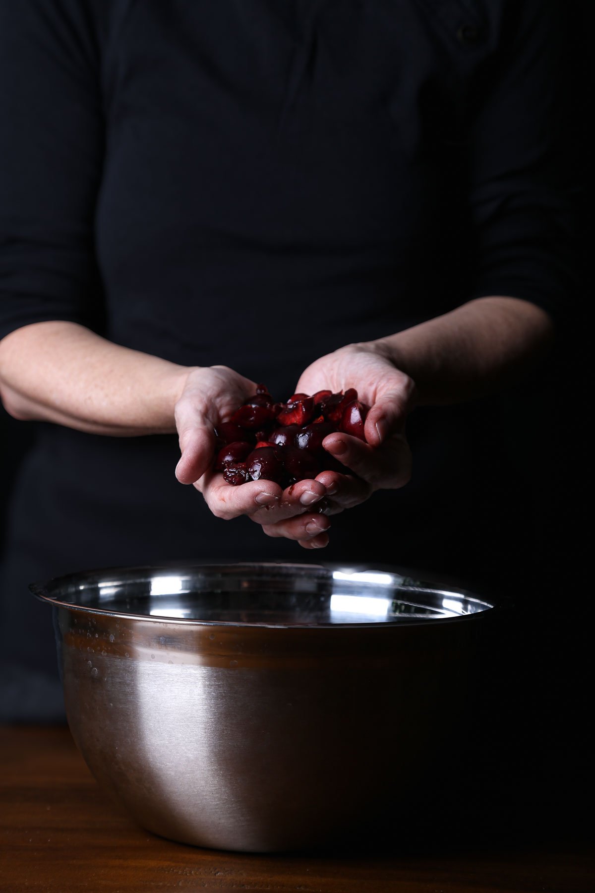 Pitted dark cherries cupped in both hands, ready to add color and depth to a berry salad.