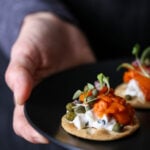A close-up shot of a carrot lox appetizer on a dark plate, against a dark background.