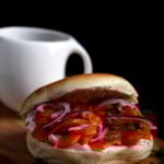 A bagel loaded with carrot lox, red onion, capers and vegan cream cheese on a wooden board.