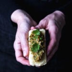 Hands holding a piece of crispy fried tofu filled with savory lemongrass-peanut sauce and garnished with cilantro.