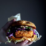 A hand holding a crispy fried tofu sandwich.
