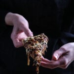 Hands holding up a slice of focaccia pizza.