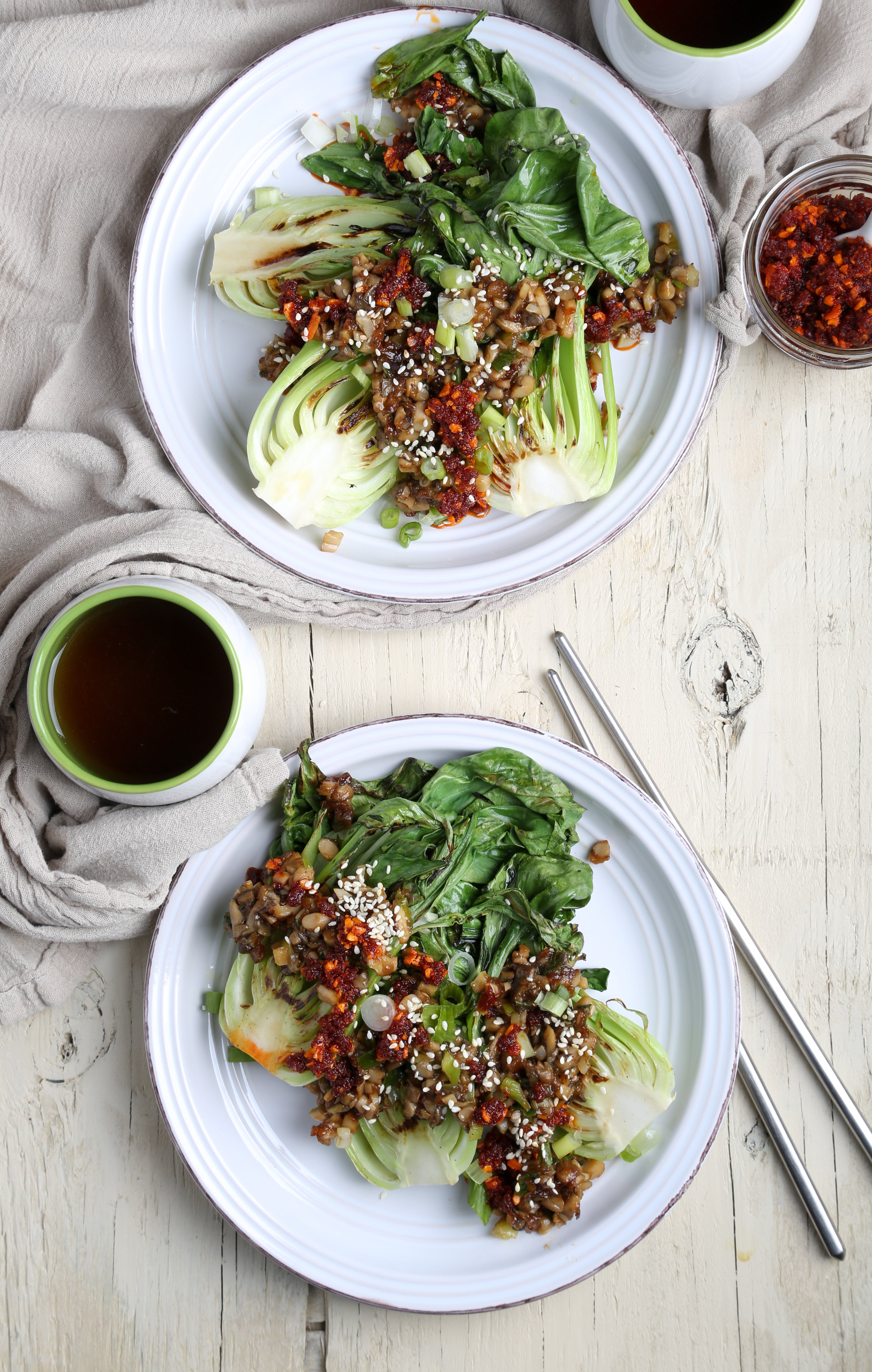 Grilled bok choy on two white plates with chopped oyster mushrooms.