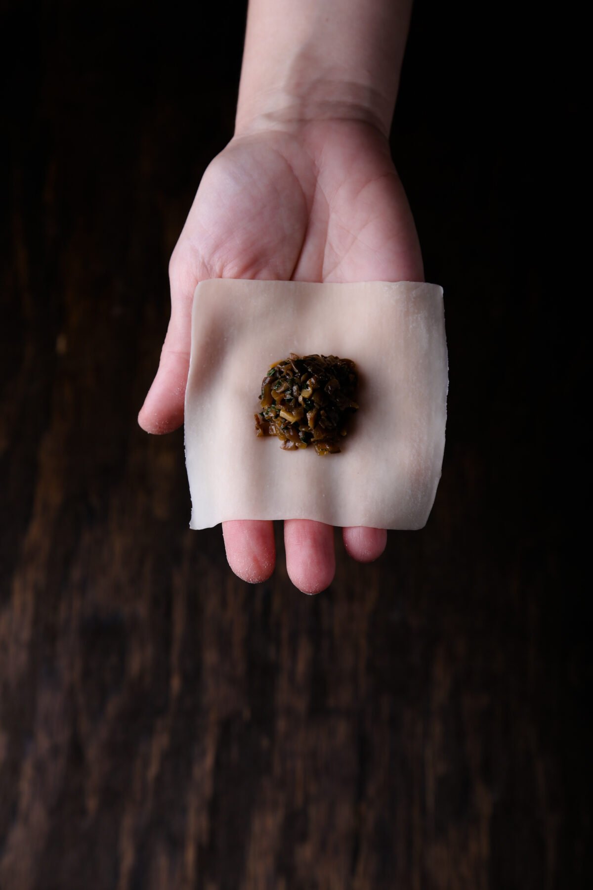 A hand holding a wonton skin with filling in the center.