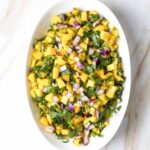 Close-up of vibrant mango salsa with cilantro and red onion in a white serving bowl.