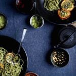 Seaweed pasta with vegan scallops served in black bowls, topped with sesame seeds and surrounded by seasoning ingredients.