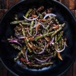 Overhead shot of spicy green beans with red onion and sesame seeds.