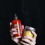 Hands holding a jar of nooch and sriracha.