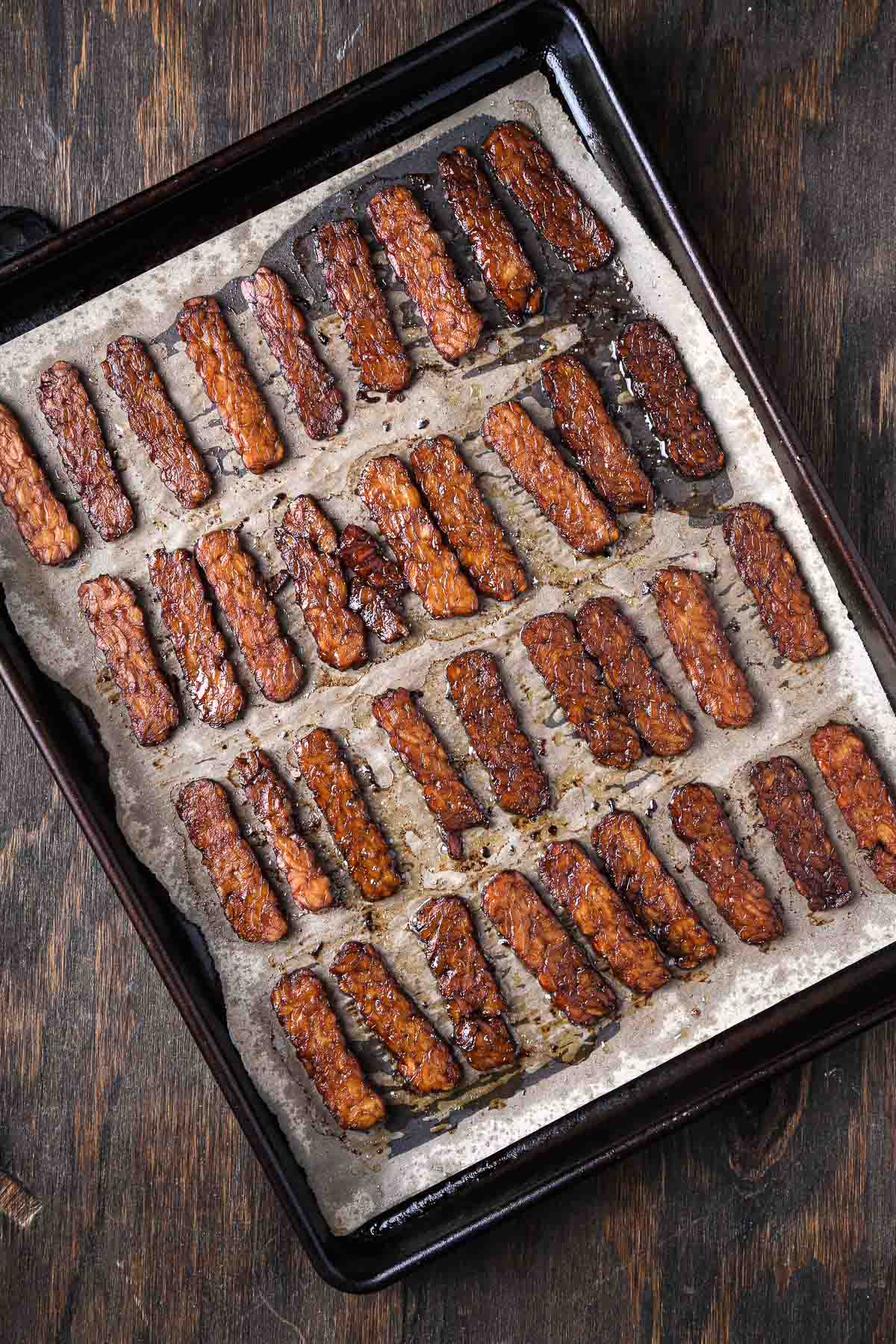 Baked tempeh bacon on parchment, golden brown and glazed with smoky marinade.