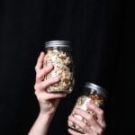 Two hands holding up jars of toasted muesli.
