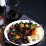 A glass of red wine beside a plate of vegan bourguignon, the ultimate slow-simmered plant-based stew for a comforting, elegant meal.
