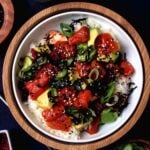 Vegan poke bowl with watermelon tuna, avocado, pickles, seaweed, and sesame seeds in a wooden bowl on a dark background.